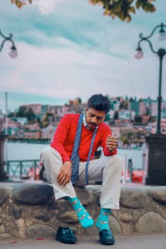 pexels-photo-1791195-1791195 Stylish man in bright attire sitting by a scenic riverfront area, exuding a modern fashion sense.