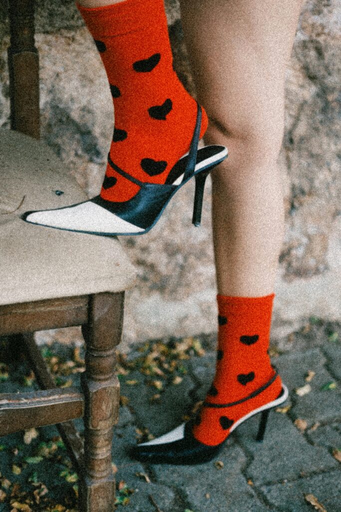 pexels-photo-28743382-28743382 Stylish red heart socks paired with black and white heels on rustic chair.