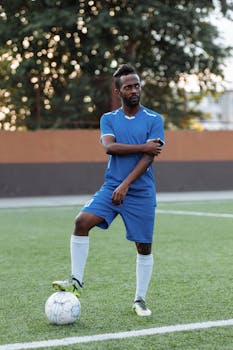 pexels-photo-5247133-5247133 Adult male soccer player in blue attire poses confidently on a green football field.