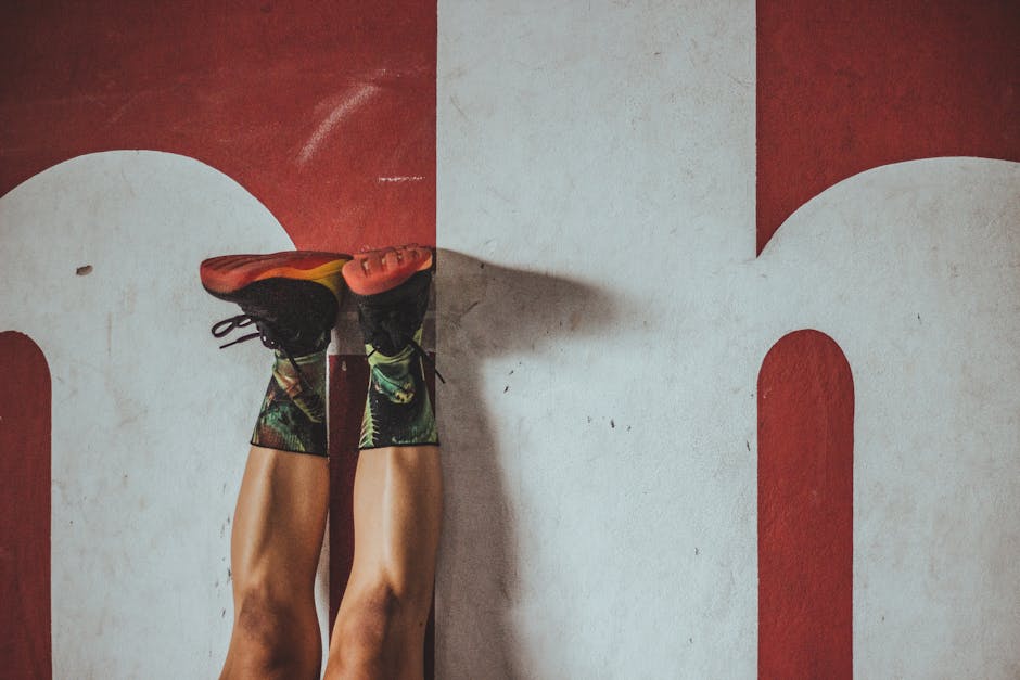 A person in colorful socks and sneakers exercising against a bold red wall.